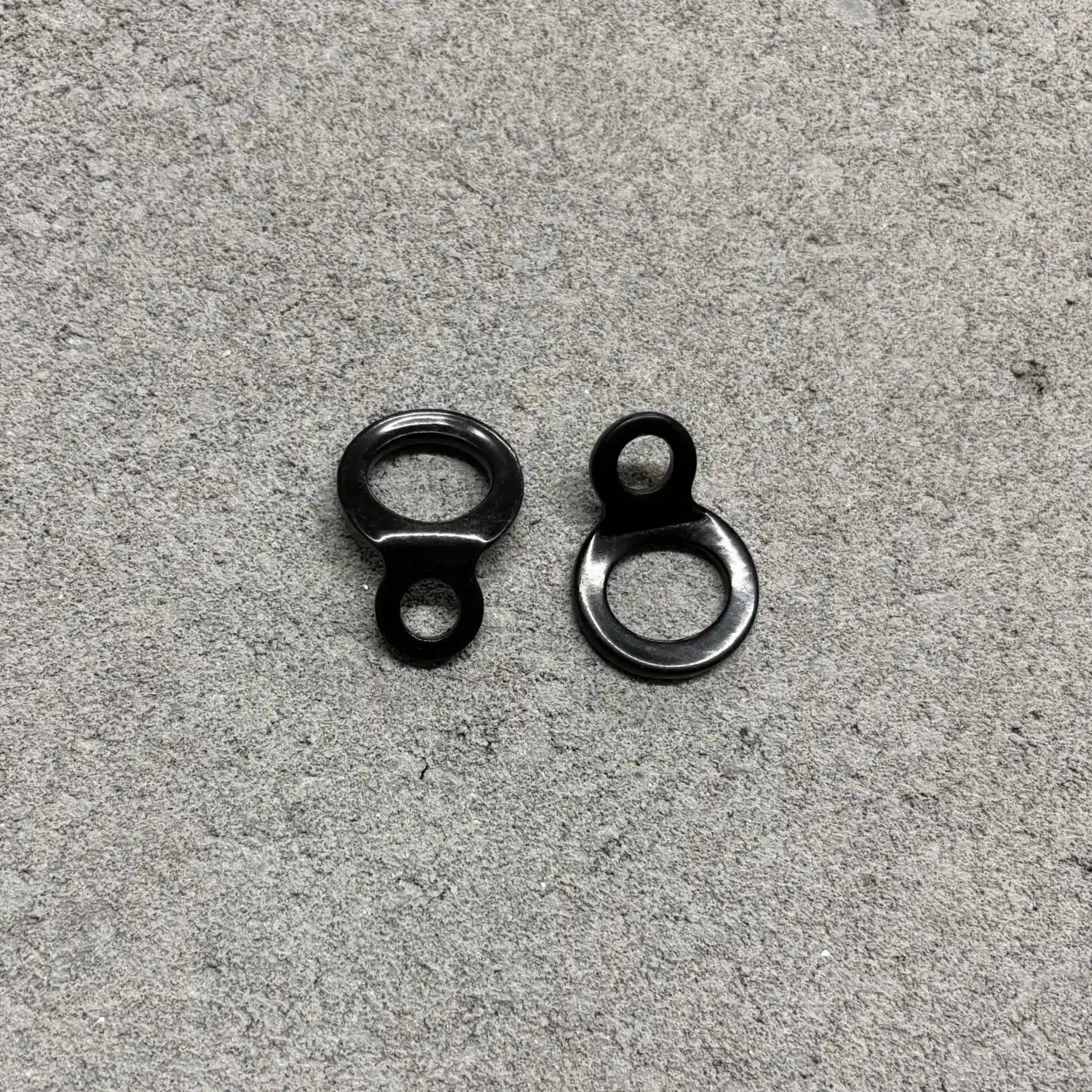 Two black metal eyelets on a gray concrete surface